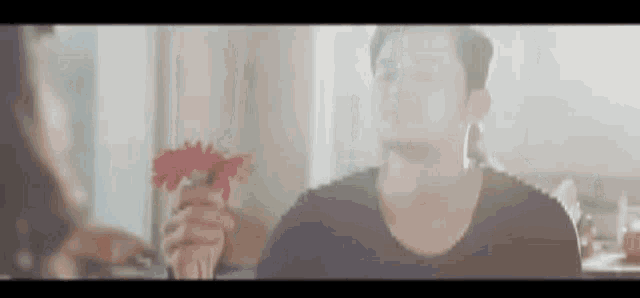 a man is holding a red flower in his hand while sitting at a table .