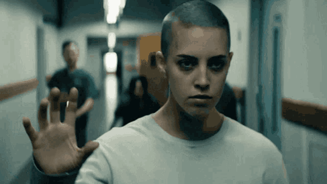 a woman with a shaved head is standing in a hallway with her hand out