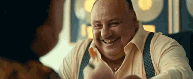 a man in a yellow shirt and suspenders is smiling while talking to a woman .