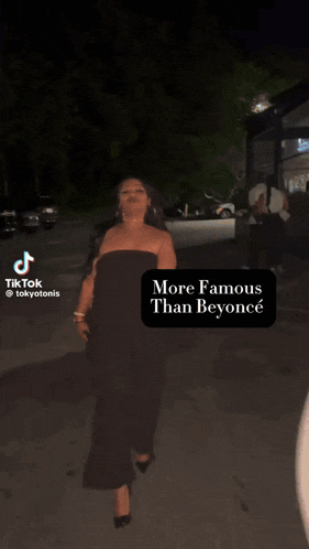 a woman in a black jumpsuit is walking down a street at night with a caption that says more famous than beyonce