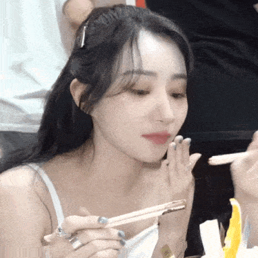 a woman in a white tank top holds chopsticks in her hand