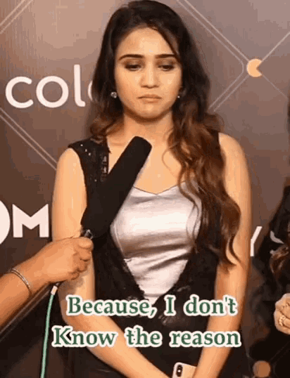 a woman talking into a microphone with a caption that says because i don t know the reason