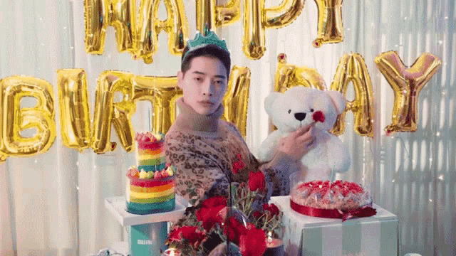 a man is holding a teddy bear in front of a happy birthday sign .