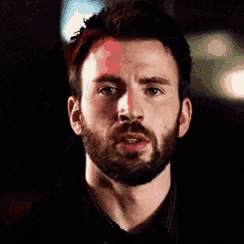 a close up of a man with a beard making a funny face in a dark room .