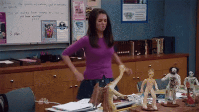 a woman in a purple shirt is standing in front of a desk with sculptures on it ..