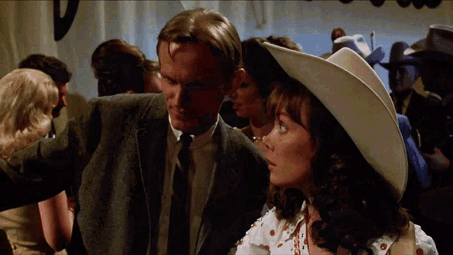 a man in a suit and tie stands next to a woman in a white cowboy hat