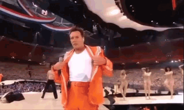 a man in an orange suit and white shirt is standing on a stage