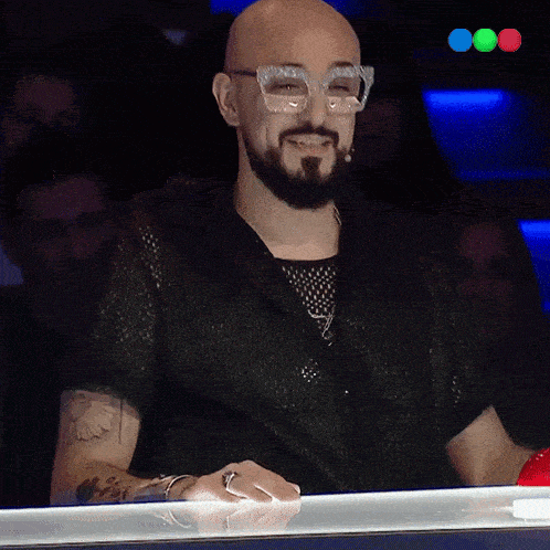 a man with glasses and a beard is smiling in front of a crowd