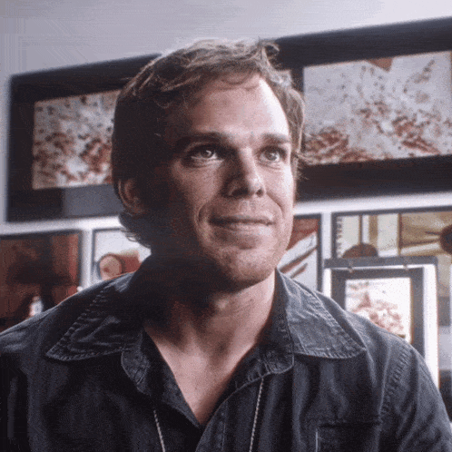 a man in a black shirt is smiling in front of a wall of framed pictures