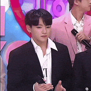 a man in a suit is talking into a microphone while standing next to another man in a pink suit .