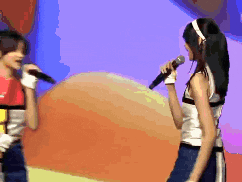 a woman singing into a microphone while another woman stands behind her
