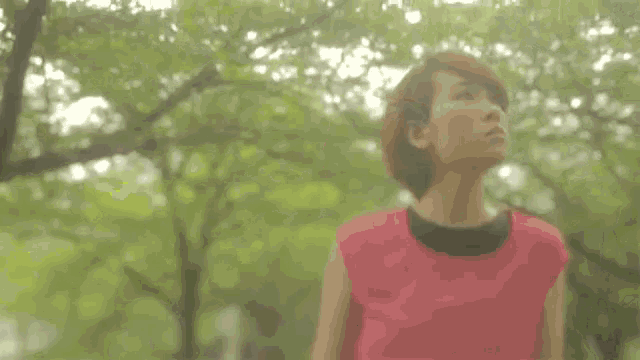 a woman in a pink shirt is standing in front of a forest .