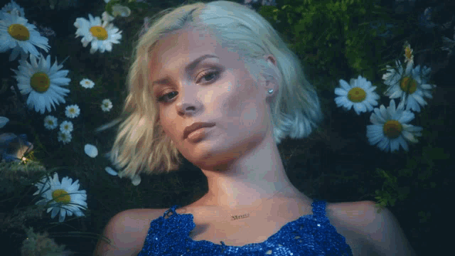 a woman in a blue dress is surrounded by daisies and has a necklace that says ' sydney ' on her chest