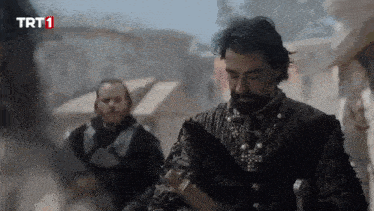 a man with a beard is holding a sword in front of a sign that says trt 1