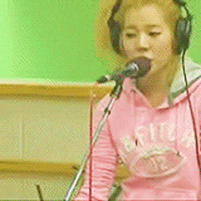 a woman in a pink hoodie is singing into a microphone .