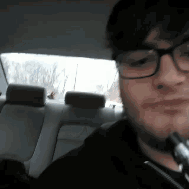 a man wearing glasses and a black shirt is sitting in the back seat of a car