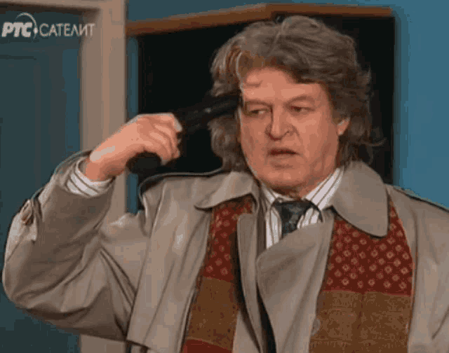 a man in a trench coat and tie is holding a gun to his head