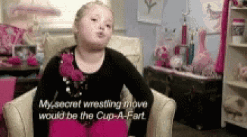 a little girl is sitting in a chair with the words " my secret wrestling move would be the cup-a-fart " on the screen