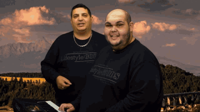 two men wearing black lifestyle shirts are playing a keyboard