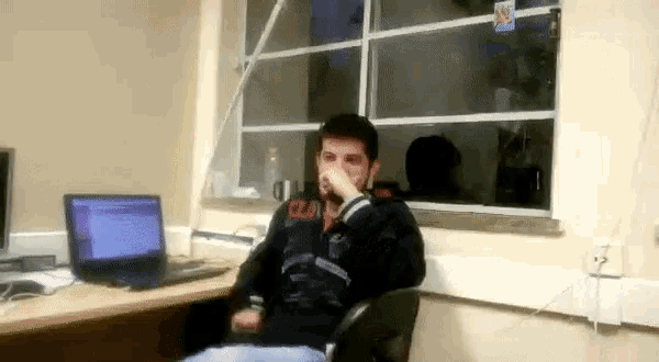 a man sitting at a desk with a laptop and a sticker on the wall that says ' coca cola ' on it