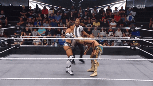 two women are wrestling in a wrestling ring with a referee in front of a crowd that says cw