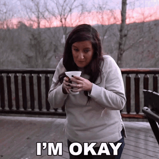 a woman holding a cup of coffee with the words " i 'm okay " below her
