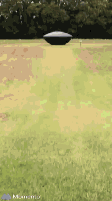 a picture of a ufo flying over a grassy field with the word momento at the bottom