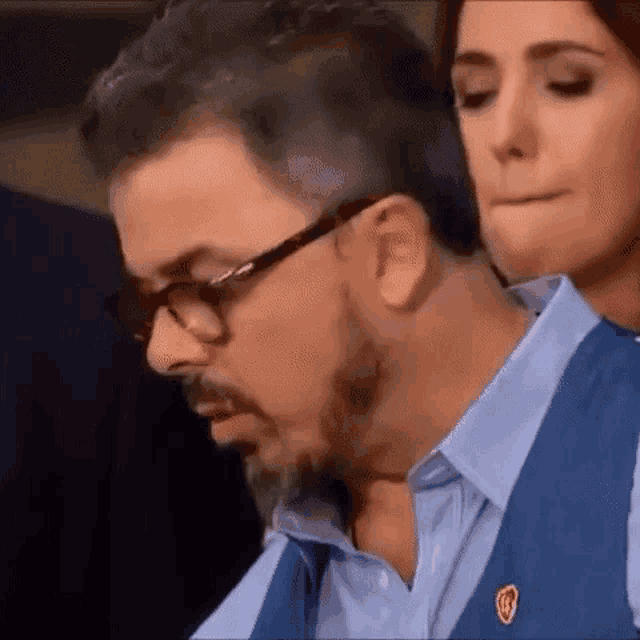 a man with a beard and glasses is sitting next to a woman in a blue shirt .