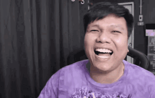 a man wearing a purple shirt is laughing with his mouth wide open
