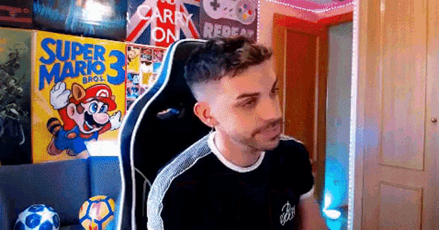a man is sitting in a chair in front of a super mario 3 poster on the wall .