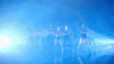 a group of people are dancing in a dark room with blue lights behind them