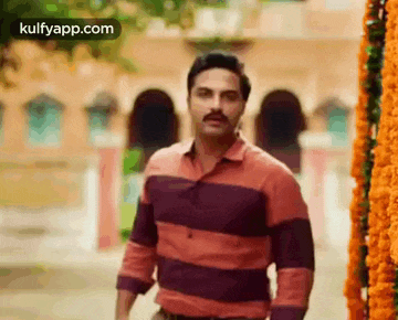 a man with a mustache and a striped shirt is standing on a street .
