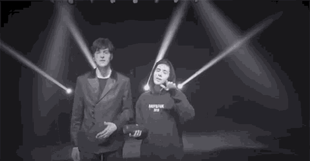 a man in a suit and a man in a hoodie are standing in front of a stage .