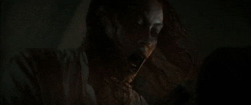 a woman with blood on her face is holding a spoon in her mouth in the dark .