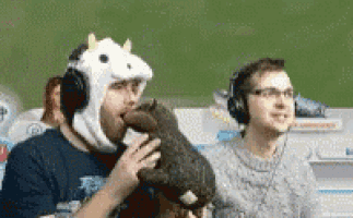 a man in a cow hat is kissing a stuffed animal while another man looks on .