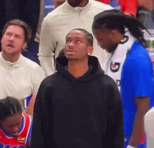 a man in a black hoodie is standing in front of a group of people .