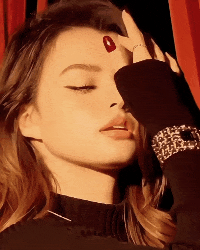 a close up of a woman 's face with a red nail on her forehead
