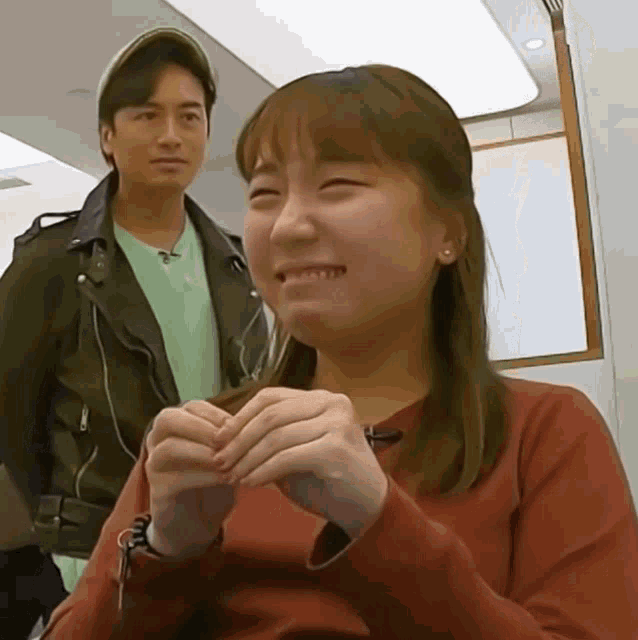 a man in a hat stands behind a woman in a red sweater
