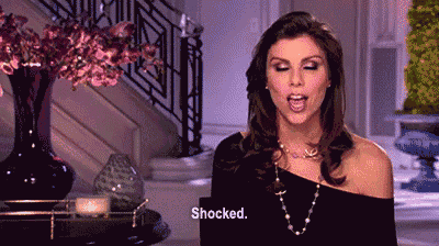 a woman in a black dress and pearl necklace says shocked
