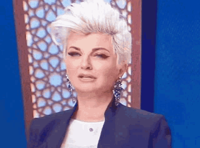 a woman with a mohawk and earrings is making a funny face in front of a blue wall .