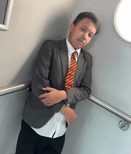 a boy in a suit and tie leans against a wall