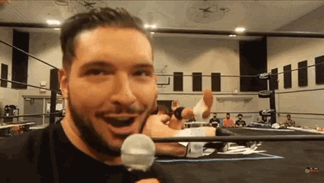 a man in a wrestling ring is holding a microphone and smiling
