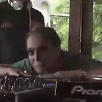 a man in a green shirt is sitting at a pioneer dj mixer .