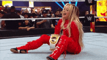 a woman in a red outfit is sitting on the ground holding a wrestling belt