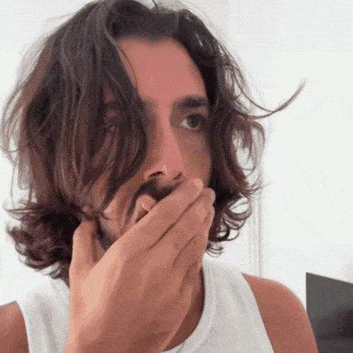 a man with long hair and a beard covers his mouth with his hand