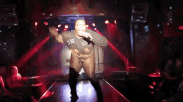 a man singing into a microphone on a stage with a red exit sign behind him