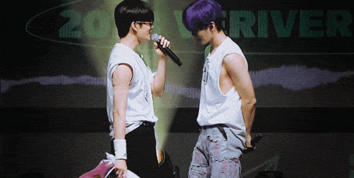 a man with purple hair stands next to another man holding a microphone in front of a sign that says river