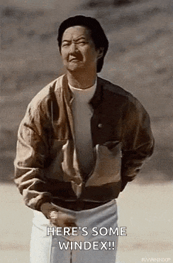 a man in a brown jacket is standing on a field with his hands in his pockets and making a funny face .