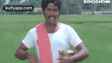 a man in a white shirt and red sash is standing in a field holding a bucket .