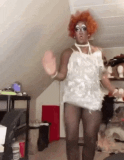 a drag queen with red hair is dancing in a room
